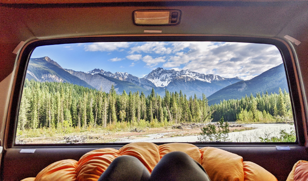 person laying in back of vehicle looking out back window to view of mountains