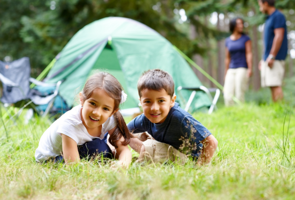 two children sitting in the grass in front of a tent