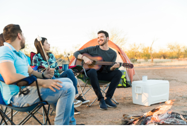 A person playing guitar around a group at a campfire