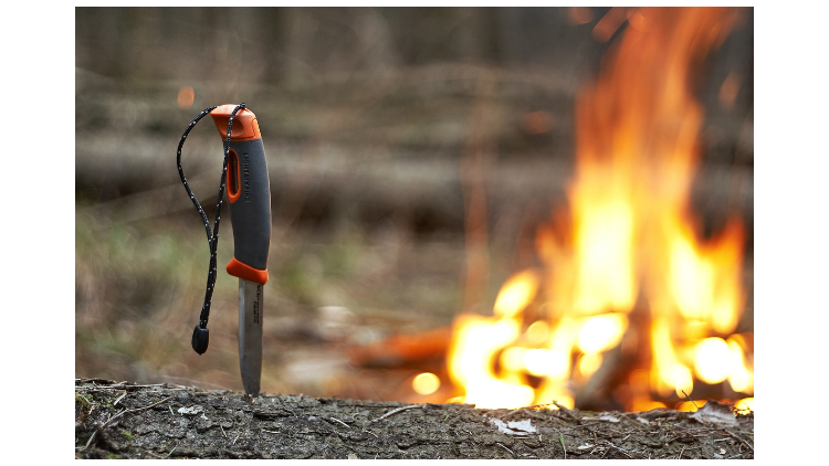 knife sticking into a log next to a campfire