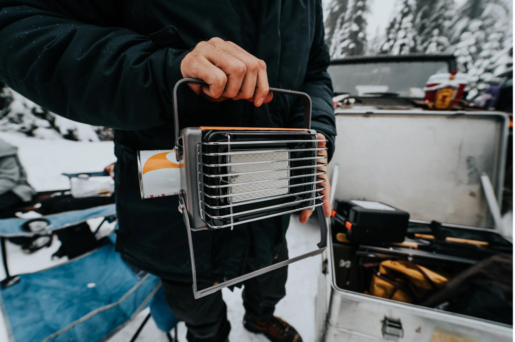 A person holding a portable heater at a campsite