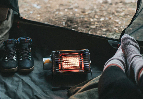 person inside tent warming feet by portable heater.