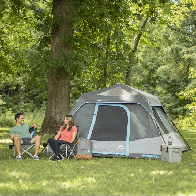 A couple sitting in chairs next to a pop up tent and trees