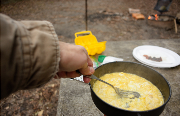 A person cooking scrambled eggs outside