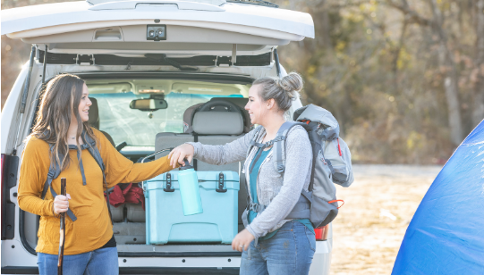 two women holding cooler on back of vehicle