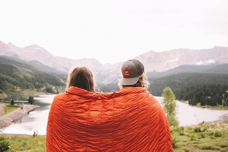 Two people sitting on a hill looking at a lake